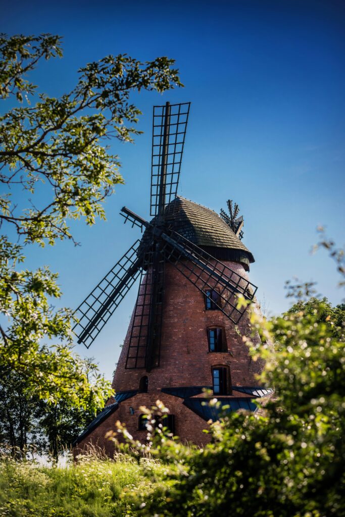 A picturesque brick windmill surrounded by lush greenery under a bright blue summer sky in Poland.