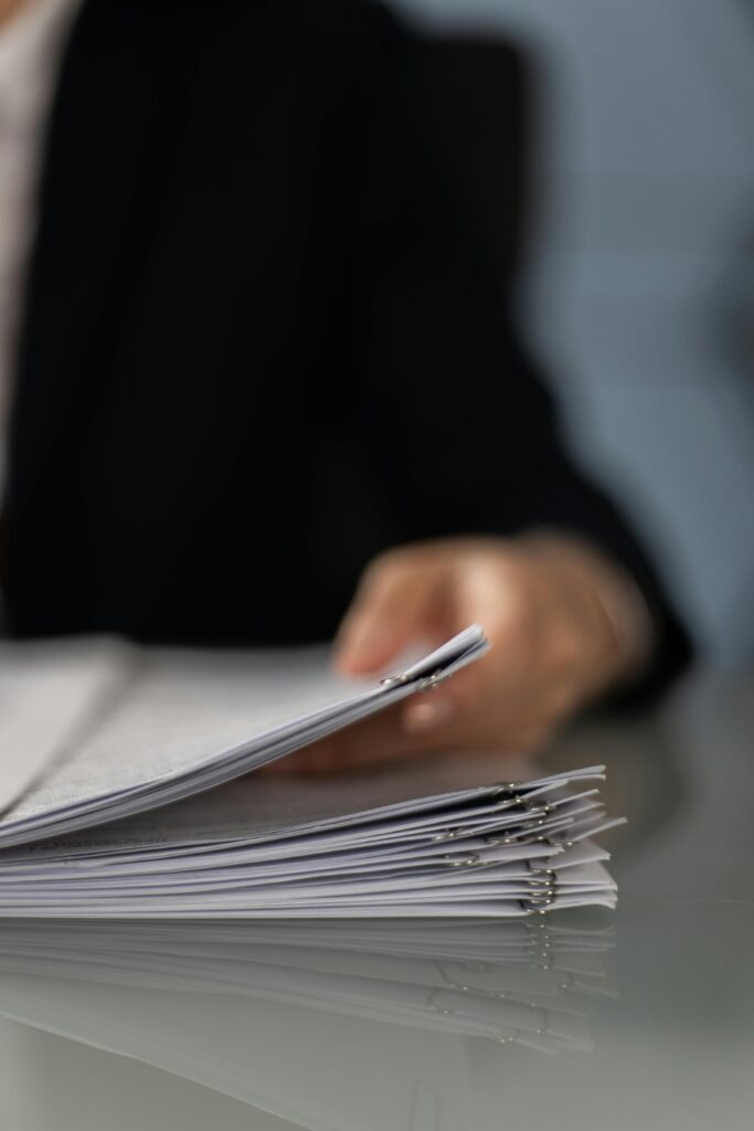 Blurred hand holding a stack of documents on a glass desk with focus on papers.